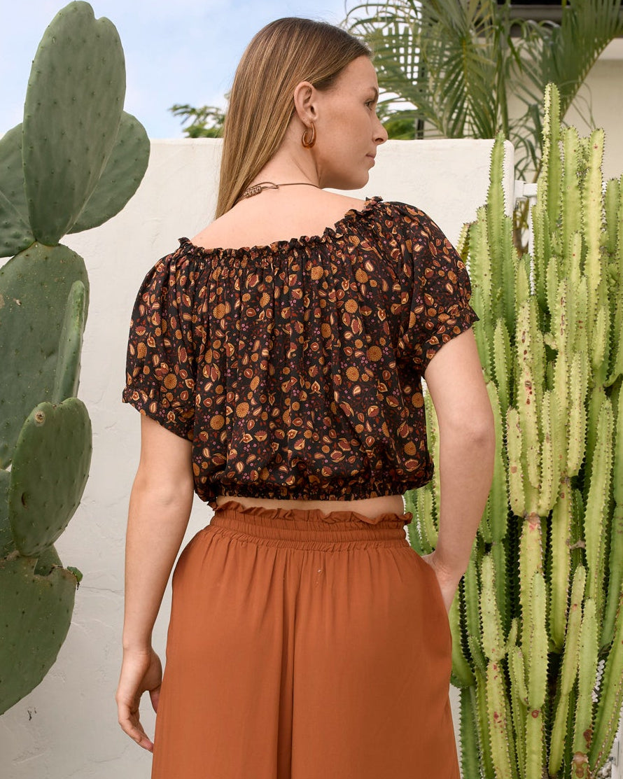 woman wearinf bohemian crop top elastic rushed neckline in black boho base with earhy florals pair with gingerbread rayon billy pants back veiw