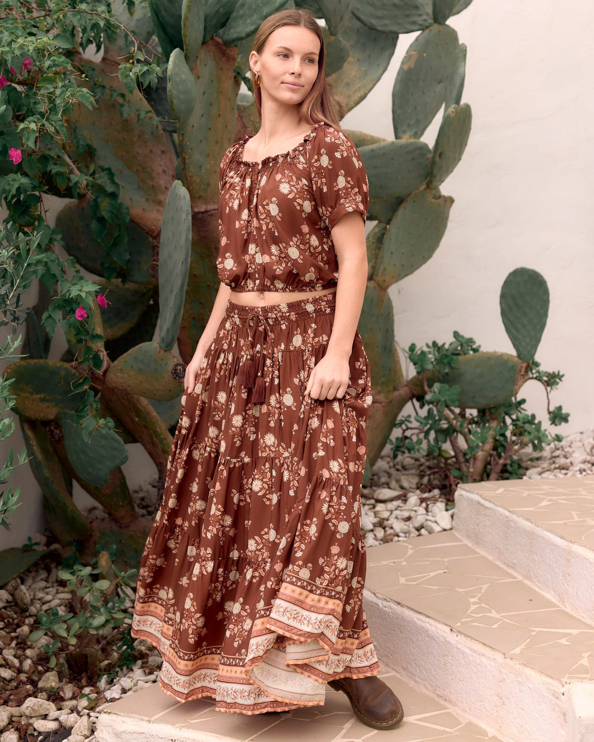 woman wearing ruched elastic neckline, soft elastic at hemline kai crop top with cuffed sleeve, brass buttons at neckline in bohemian brown floral dahlila print with matching oakley tired maxi skirt front view