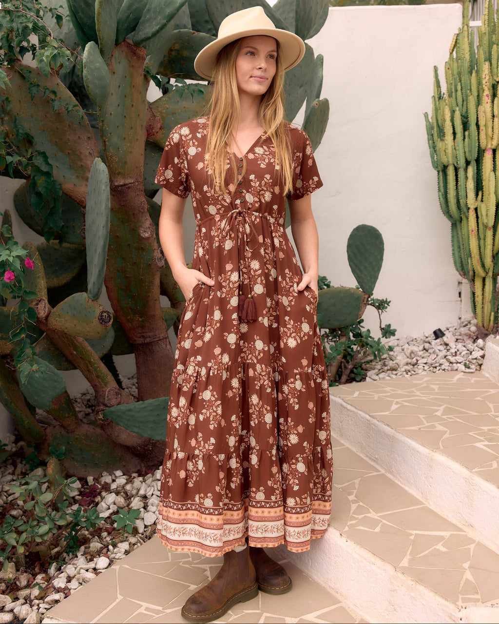 A woman wearing mandy maxi dress in brown bohemian floral dahlila print with a tie-front V-neck, short sleeves, and oatmeal felt isla hat