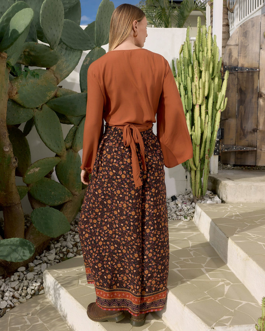 A woman viewed from behind wearing fae tie top gingerbread and rio pant la luna black base floral pant with orange and mustard patterned details